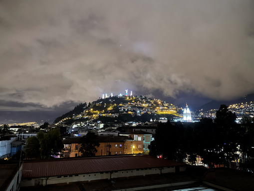 Distant view of El Panecillo hill in Quito at night, with glimmering city lights beneath the Virgen del Panecillo statue