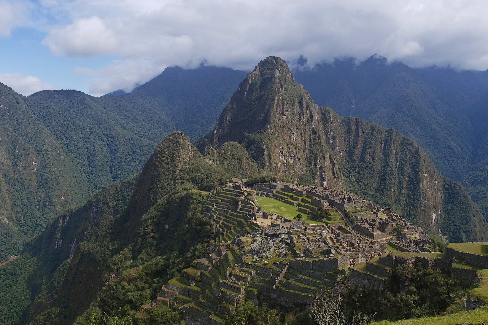 Looking down at the terraces and stone structures of Machhu Picchu, with the towering Huayna Picchu summit looming over the ruins