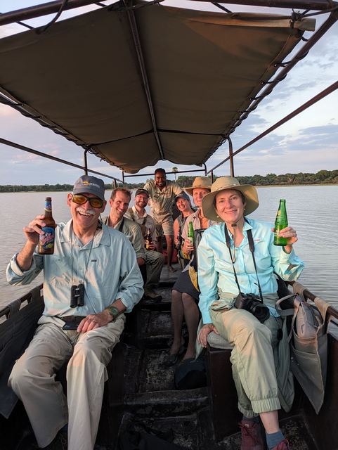 Safari guests toast raise their glasses during a sunset boat cruise on a luxury safari from Roho ya Selous Camp in Nyerere National Park (the Selous) Tanzania