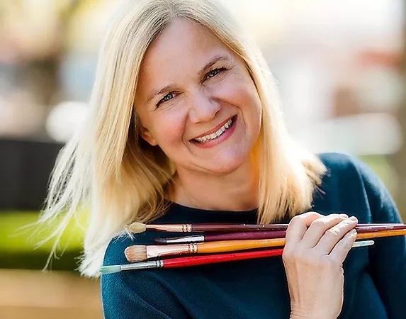 Artist Britt Greenland smiling and holding paintbrushes