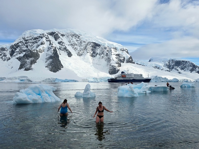 two women polar plunge in the icy waters of Antarctica with their crusie ship behind them
