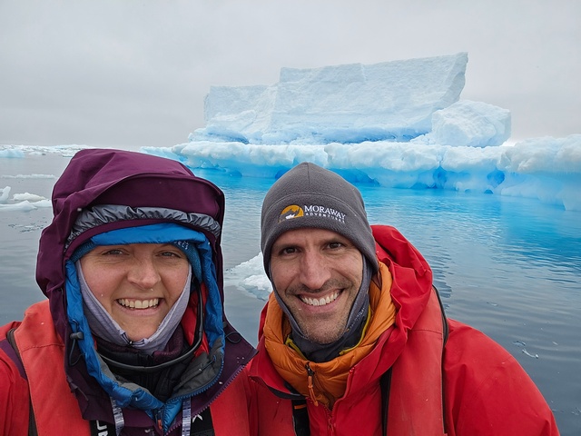 two antarctica cruise passengers smiling in front of an iceberg