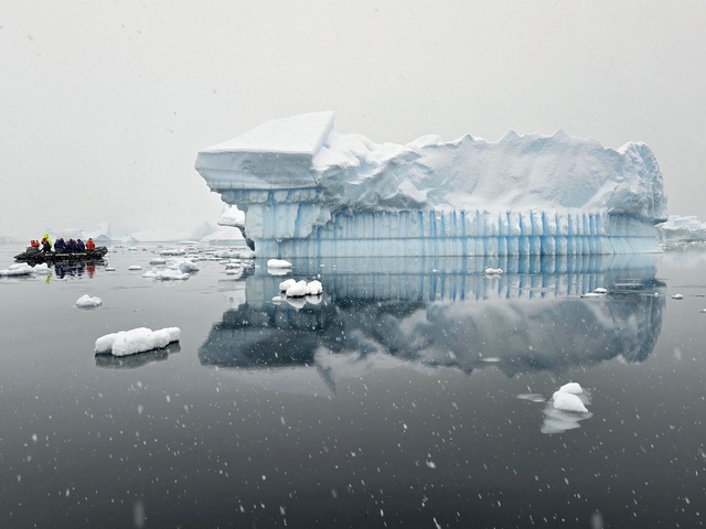 a zodiac boat dwarfed by a massive iceberg reflecting in the waters of Kinnes Cove Antarctica