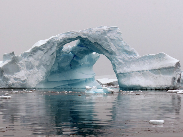 a massive iceberg with an arch shape to it in the waters of kinnes cove antractica