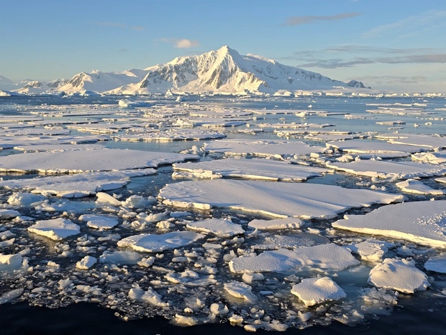 sea ice breaking up in the waters of the Antarctic Circle, with a huge mountain in the background