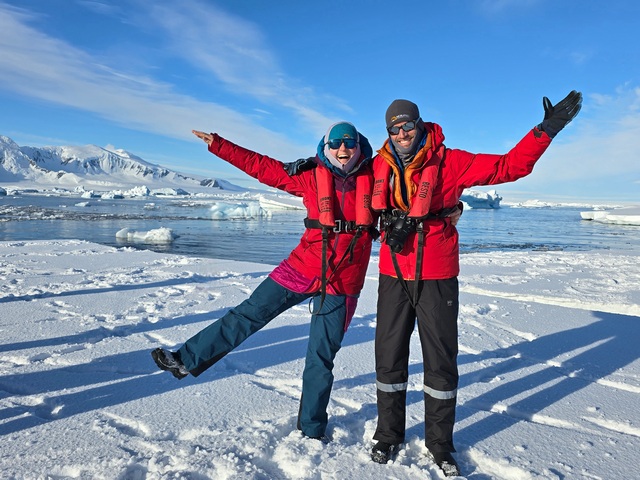two smiling people standing on a sheet of sea ice at the Polar Circle of Antarctica, on a beautiful sunny day