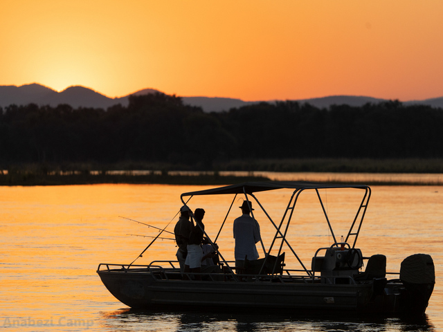 Guests fishing from a small boat at sunset while on a luxury safari at Anabezi Camp in the Lower Zambezi, Zambia