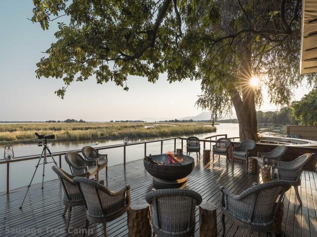 The setting sun behind a beatiful tree framing an outdoor seating area along the river at Sausage Tree, a luxury safari camp in the Lower Zambezi, Zambia