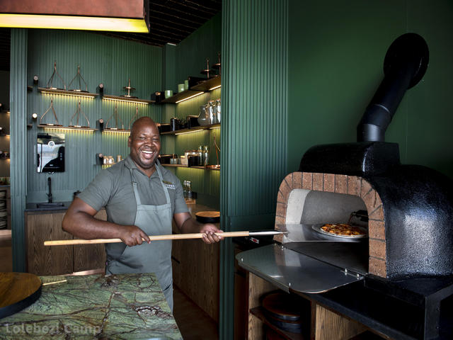A smiling chef removes a pizza from a pizza oven at Lolebezi Camp in the Lower Zambezi National Park, Zambia