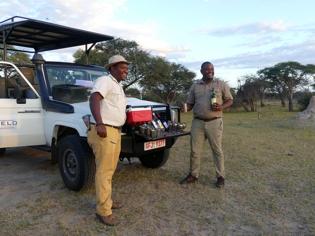 Two smiling guides serving sundowner cocktails off the front of a safari vehicle during a luxury safari in Hwange National Park