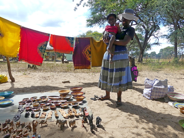 A mother holds her baby while standing next to the curios she sells to visitors on safari in Hwange National Park Zimbabwe