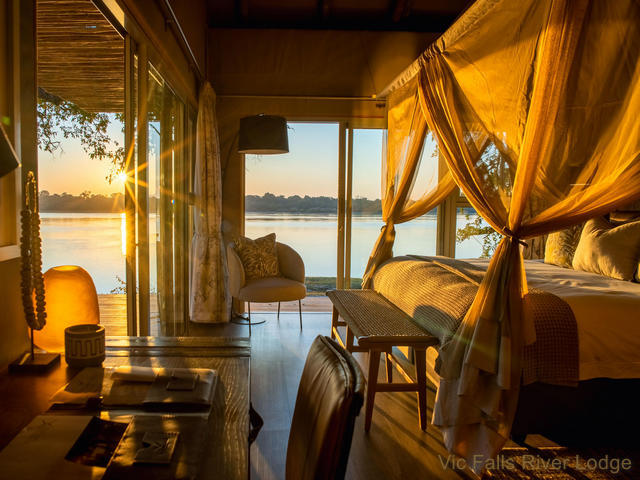 View of the inside of a luxury chalet at Victoria Falls River Lodge as the sun sets over the Zambezi River outside