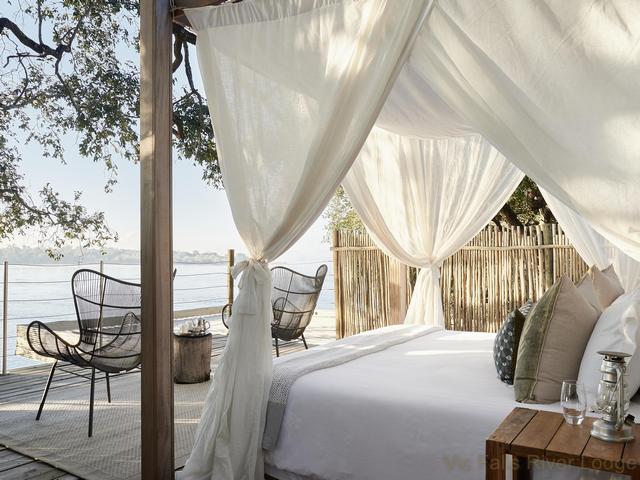 View of the canopied bed and outdoor sitting area of a luxury chalet at Victoria Falls River Lodge on the Zambezi River