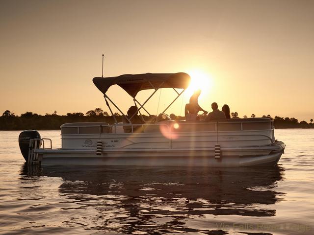 A small boat cruising along the Zambezi River at sunset during a luxury safari at Victoria Falls River Lodge