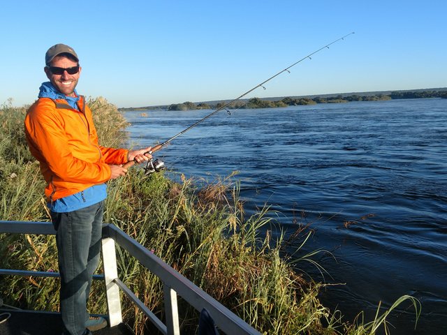 A smiling safari guest fishing for Tiger Fish in the Zambezi River during a luxury safari at Victoria Falls River Lodge