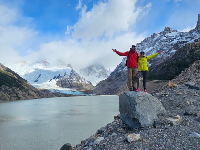 Two hikers standing tall on a rock with a mountain lake in the background while hiking the Laguna Torre hike near El Chalten in the Patagonia region of Argentina