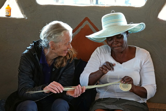 a zimbabwean woman shows a tourist how to weave grass into a basket