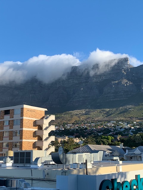 Clouds spilling over the top of Table Mountain with a blue sky up above