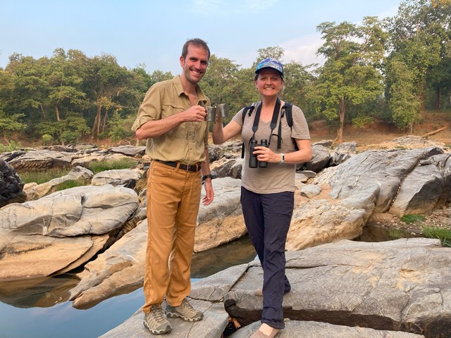 A couple on a luxury tiger safari in India enjoying chai tea as they stand alongside a river at Kanha Jungle Lodge