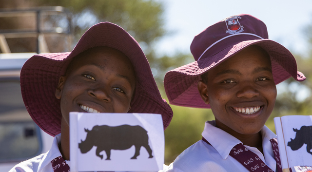 Two smiling young women from the local community hold up flags to celebrate the reintroduction of white rhinos in Hwange National Park