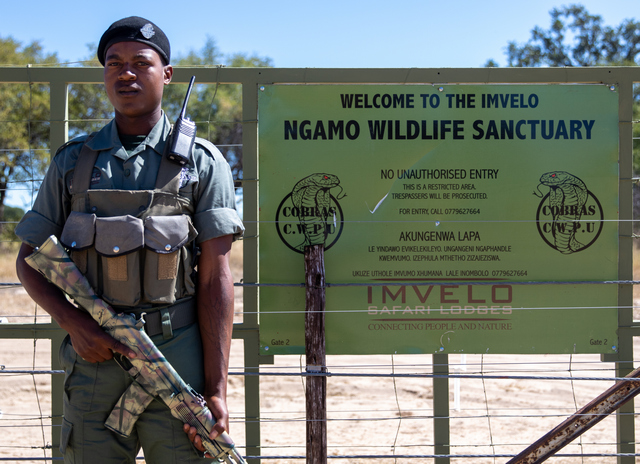 An armed ranger standing next to the welcome sign for the Ngamo Wildlife Sanctuary in Hwange National Park Zimbabwe