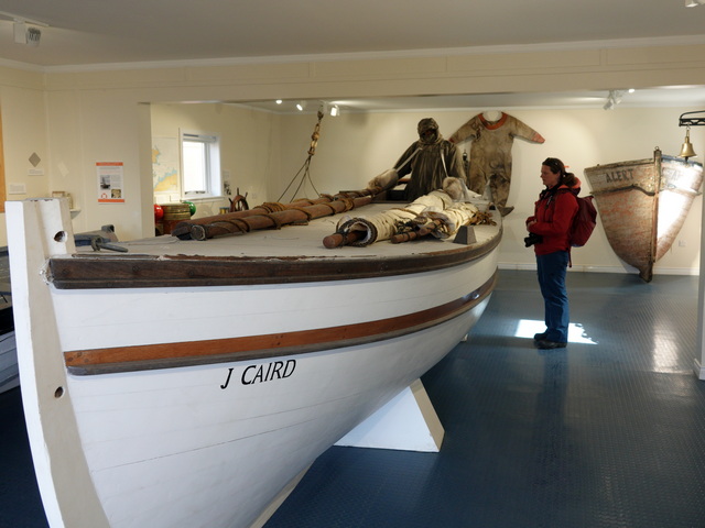 A visitor stands next to a life-sized replica of the James Caird in the museum at Gritviken