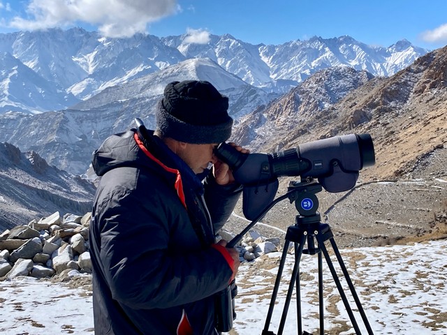 A spotter from Snow Leopard Lodge in Ulley, India looks through a spotting scope, searching for snow leopards in the mountains above