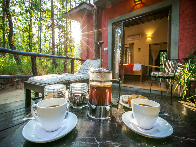 Breakfast table set with french press coffee and mugs on an outdoor patio at a luxury safari camp near Bandhavgarh Tiger Reserve in India
