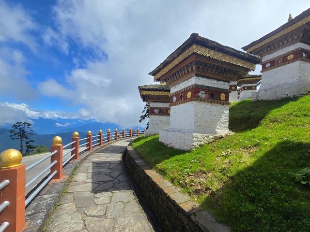Ornate chortens with blue skies and views of Himalayan peaks behind them at Dochula Pass, Bhutan