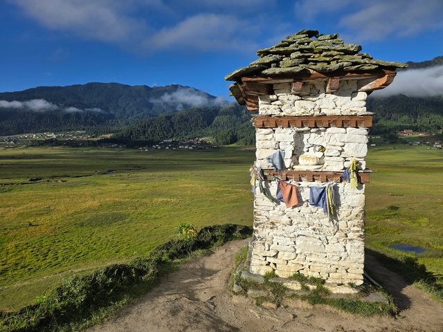 A slightly worn chorten with sun-bleached prayer flags, looking over the open fields of Bhutan's Gangtey valley at dawn